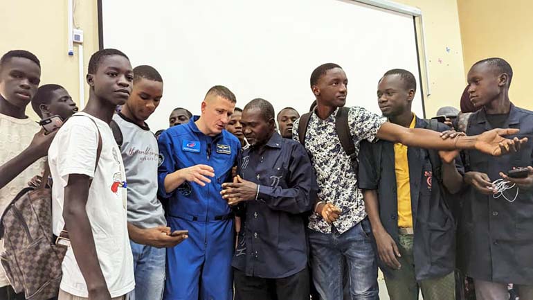 Un cosmonaute en combinaison bleue échange avec des étudiants lors d’une rencontre du projet